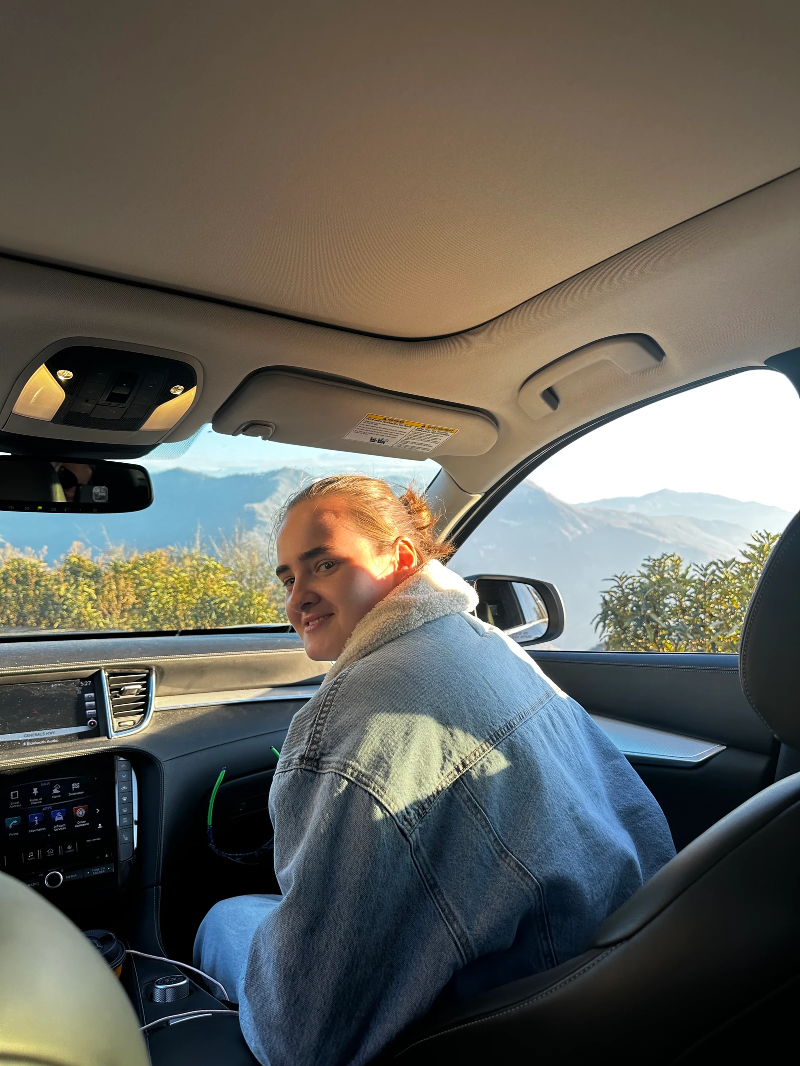 Portrait of photographer Daria Zamorskaia in a denim jacket, seated in a car in warm sunlight